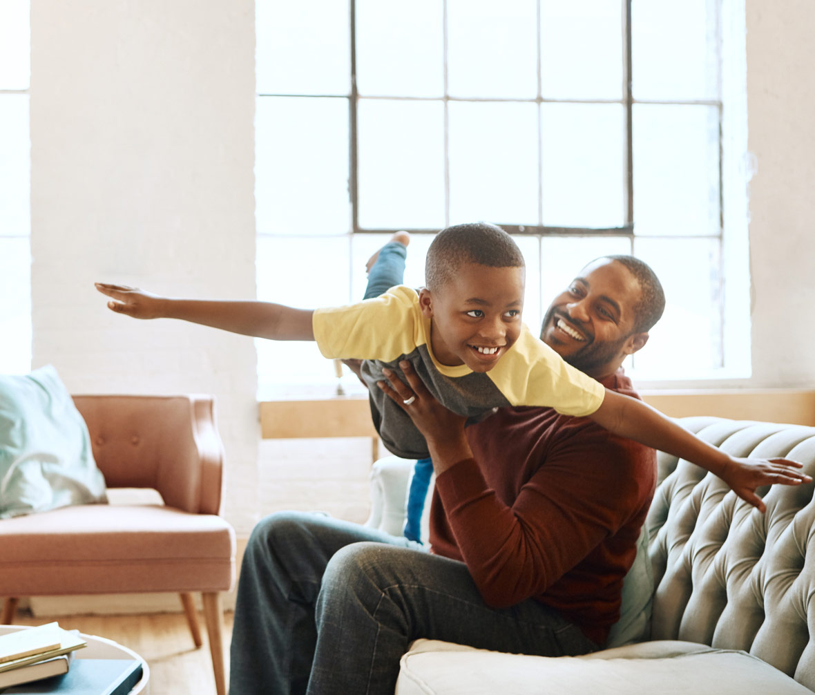 Man flying son like an airplane on the couch